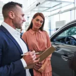 A service advisor with a clipboard explaining the differences between an extended warranty and a vehicle service contract to a car owner.