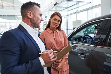 A service advisor with a clipboard explaining the differences between an extended warranty and a vehicle service contract to a car owner.