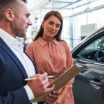 A service advisor with a clipboard explaining the differences between an extended warranty and a vehicle service contract to a car owner.