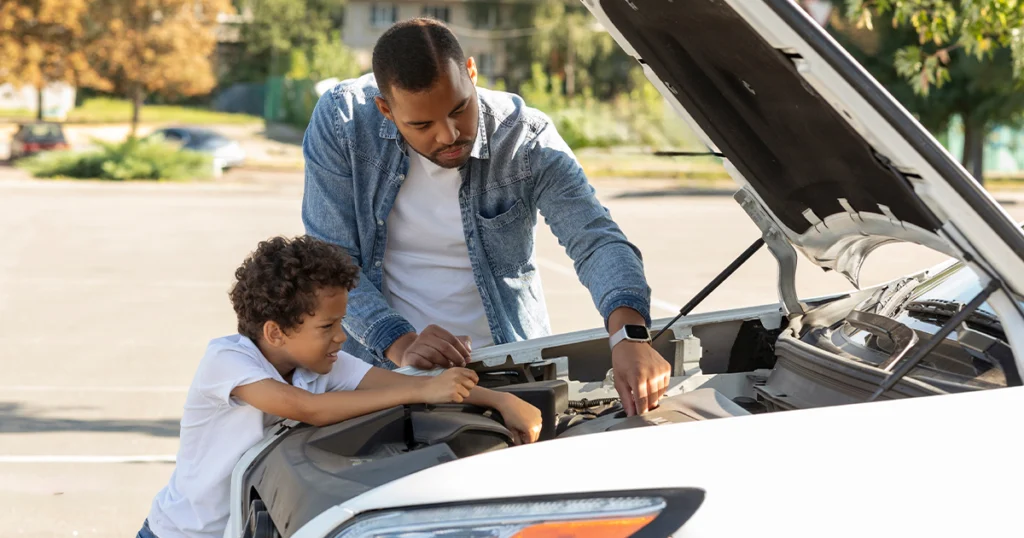 100K mile car maintenance: a child and adult checking under the hood of a car with the hood raised