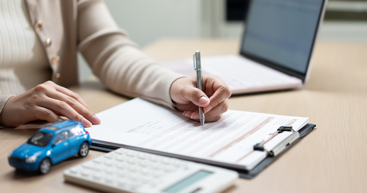 A person compares vehicle service contract quotes at a desk, with a toy car, calculator, and laptop open for research.
