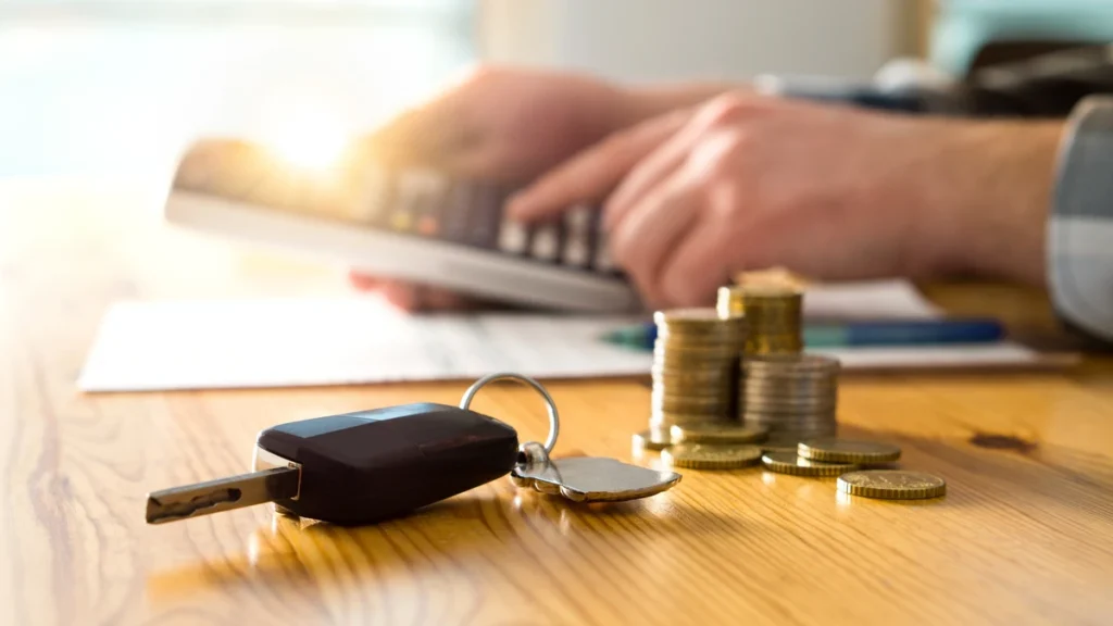 Car keys and stacked coins next to a calculator representing the cost of a vehicle service contract and protection pricing