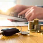 Car keys and stacked coins next to a calculator representing the cost of a vehicle service contract and protection pricing