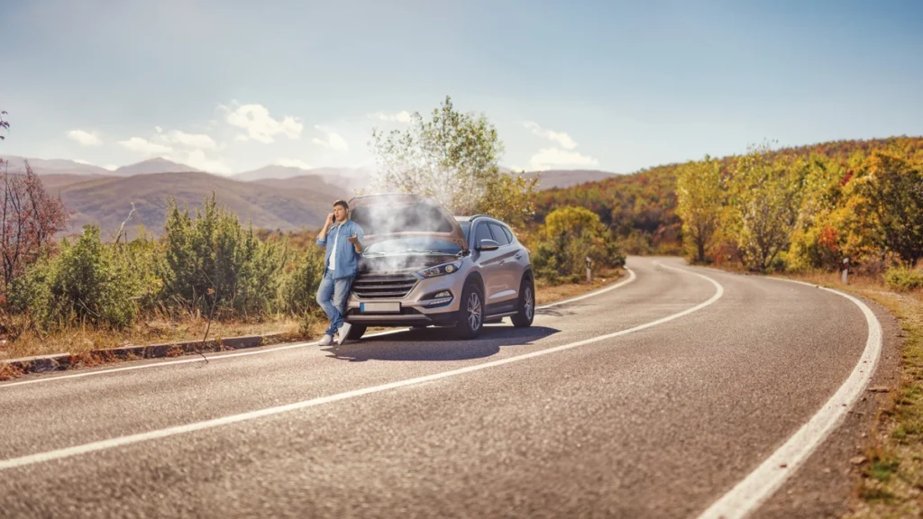Driver calling for roadside assistance next to a broken down overheating car on a rural highway after a mechanical breakdown