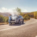 Driver calling for roadside assistance next to a broken down overheating car on a rural highway after a mechanical breakdown