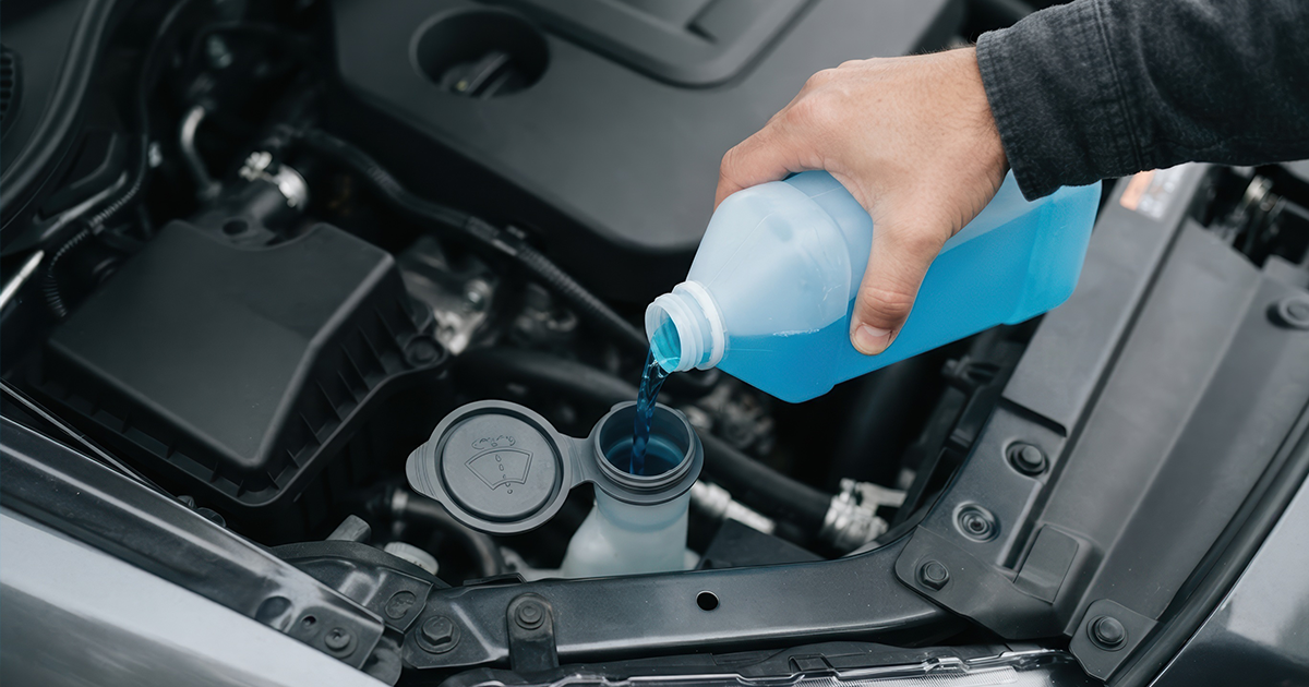Person checking engine oil dipstick under the hood of a car to check car fluids